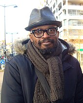 Photographie d'un homme portant des lunettes et un chapeau.