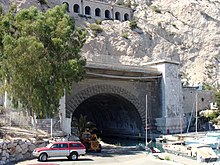 Den mørke runde åpningen av en tunnel i bunnen av en klippe, sett på avstand