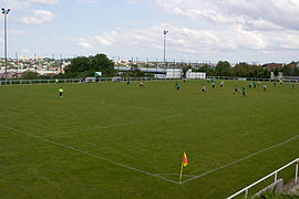 Vue d'un terrain de sport en gazon ; un match de football est en cours.