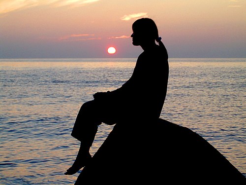 Young woman at baltic Sea coast at Sundown sitting on rock enjoying the mood