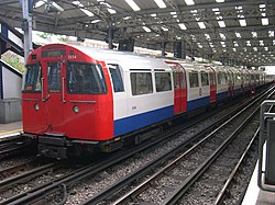 A grey, red and blue 1972 Stock Bakerloo Line train waiting at a platform at Queen's Park station, bound for Elephant & Castle