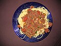 A meat sauce on spaghetti. The sauce contains tomato puree, diced tomatoes, diced beef, and bell peppers (red, yellow, and green) with the seeds included. A portion of the beef is intentionally over-cooked. The sauce is seasoned with fresh garlic, basil, oregano, paprika, onion powder, cajun seasoning, crushed red pepper, parsley, chili powder, olive oil, and possibly some additional seasonings.