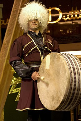 A man in a large, white hat plays a drum