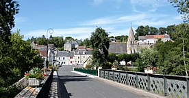 Farbfoto eines Dorfes auf der Seite eines Hügels mit einer Brücke im Vordergrund.