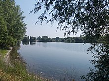 Die Kiesgrube ist heute ein naturnaher See, der von Laubbäumen gesäumt ist.
