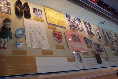 Музејска витрина која садржи фотографије, папире, ципеле, лутке те друге артефакте из Хилариног раног детињства