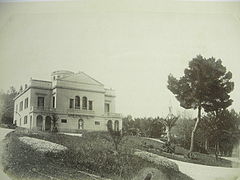 Le Plantier de Costebelle im Jahr 1863, der Park noch unberührt von Plantagen, rechts vom Haus sichtbare Taxis.  Rechts auf dem Foto eine große Aleppo-Kiefer.  Die Schotterwege und eine Kapelle im niedrigen Kiefernwald sind sichtbar.  Einige junge Phoenix Dactiliferas werden gepflanzt.