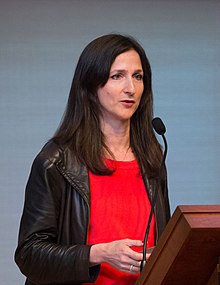 Seager speaking into a microphne, standing at a lectern