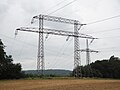 Portalmast der Werratalquerung (Nordseite), zwischen den Beinen führt ein Feldweg hindurch. Dahinter ein Mast der kreuzenden Bahnstromleitung.