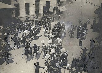 A crowd scatters in the street, with a carriage peeling away from a cloud of smoke in the background