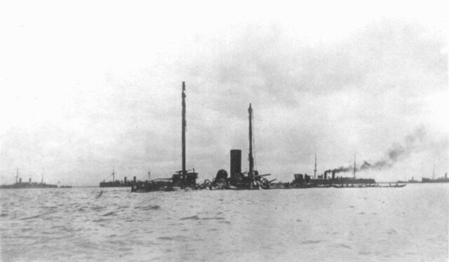 The wreck of Castilla, with Dewey's squadron and merchant ships in the background.