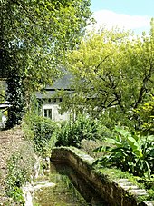 Kleurenfoto van een gebouw dat gedeeltelijk wordt verduisterd door bomen met een kanaaltje gevuld met water.