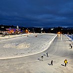 Outdoor nighttime photo of an illuminated oval with speed skaters