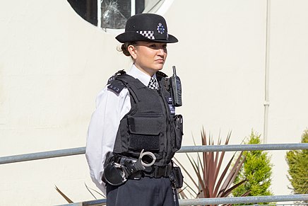 A Met Police officer in standard uniform. Female officers wear a bowler cap, as opposed to a peaked cap or custodian helmet.