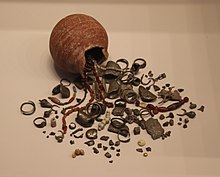 Petite jarre renversée dont l'ouverture est brisée, avec des petites objets étalés devant.