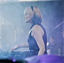 Blond kvinna bär mörk topp på scenen bakom ljudblandningsbord