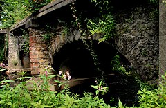 Close-up of three low stone and brick arches over running water.