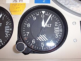Kollsman-type barometric aircraft altimeter set at 75 ft (23 m) showing a pressure of 29.87 in (1011.5 hPa). This altimeter is mounted in a console at an airfield radio station.