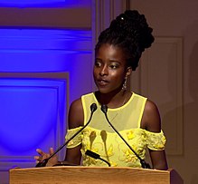 Amanda is in a bright yellow dress, standing on a stage.