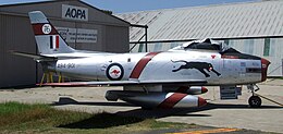 Sabre single-engined jet fighter painted silver and parked in front of a hangar