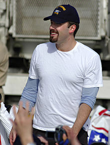 Ben Affleck, with a trim goatee and moustache, is surrounded by hands reaching out to him.