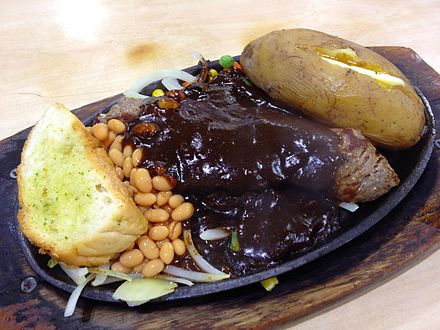Chinese style mixed grill consisting of lamb chops, chicken chops, beef steak, baked potato, baked beans and garlic toast topped with black pepper sauce.