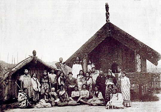 Photo posée d'un groupe devant une maison traditionnelle maorie.