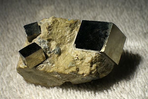 A rock containing three crystals of pyrite (FeS2). The crystal structure of pyrite is primitive cubic, and this is reflected in the cubic symmetry of 