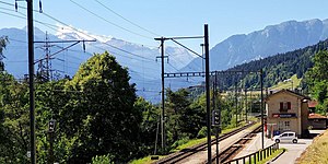 Dağ vadisinde, çift hatlı demiryolu hattının yanında yer alan üçgen çatılı iki katlı bina