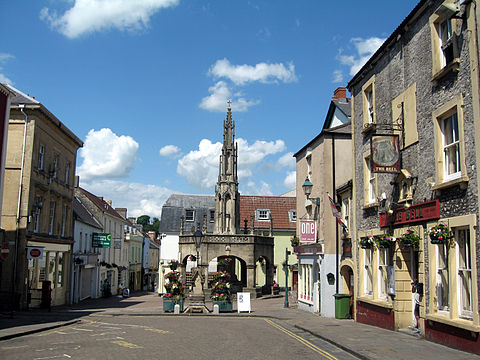 Street scene with buildings on the left and right. In a central position is a stone arched building with a spire.