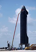 Workers near a tall spacecraft with heat shield