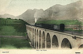 Carte postale en couleur du représentant le viaduc ferroviaire dans une vue à niveau, avec un train à vapeur le traversant, vers le tournant du XXe siècle. .