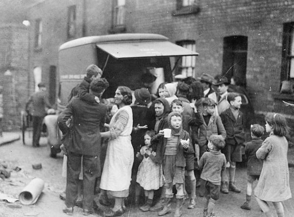 Mothers and children in a working class area of Swansea have tea and sandwiches from a mobile canteen after a night's bombing.