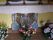 Kamenná doska z erbom oprená o stenu obklopená kvetinami v kvetináčoch.