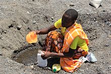 A woman digs in a dry stream bed in Kenya to find water during a drought. Digging for drinking water in a dry riverbed (6220146368).jpg