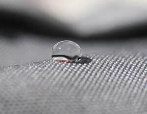 side view of a drop of water on a gray cloth. Looks like about a 120 degree angle.