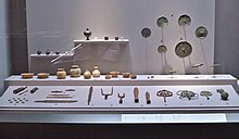 Farbfoto von alten Gegenständen (Keramik, Werkzeuge, religiöse Verzierungen), die hinter einem Fenster angezeigt werden.