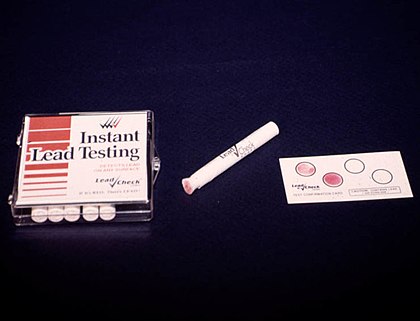 A box of cigarette-like white cylinders on the left, in the middle a white cylinder with a pink tip, on the right a paper with four circles, two blank and two pink
