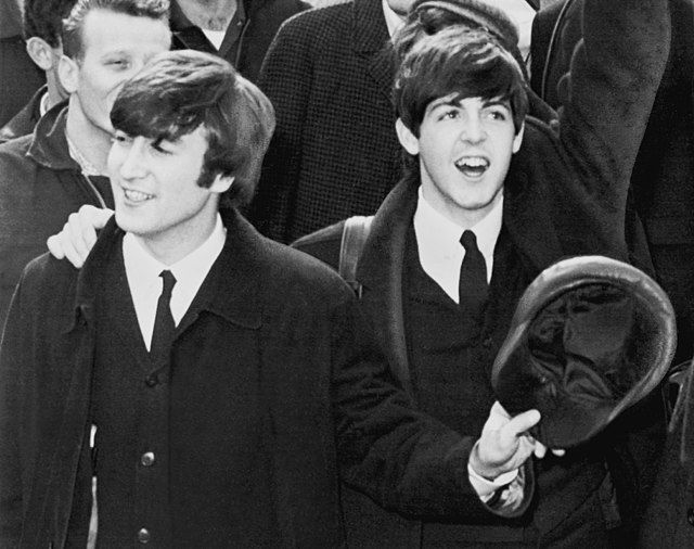 Photo en noir et blanc de John Lennon et Paul McCartney saluant une foule