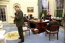 George H. W. Bush, sitting at the C&O desk, speaks on the phone with John Major while Colin Powell uses a secondary phone stored in one of the desk's drawers to speak with Norman Schwarzkopf. President George H. W. Bush speaks by phone with British Prime Minister John Major.jpg