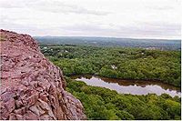 Utsikt over en steinete klippe med utsikt over en skog og dam