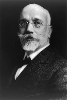 Photographie en noir et blanc d'un homme chauve, portant une barbe blanche et des lunettes.