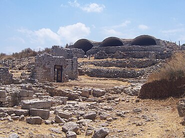 fotografia di rovine: mura, sullo sfondo un grande edificio a tre volte