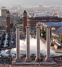 Las Cuatro Columnas, que simbolizan las cuatro barras de la señera catalana, junto a la Fuente Mágica de Montjuic. Al fondo las Torres venecianas y la antigua plaza de toros Arenas de Barcelona