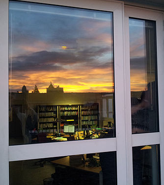 Reflet d'un coucher de soleil dans une vitre se superposant au plafond du bureau à l'intérieur.