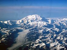 Auf einem Luftbild ist ein Berg von vielen kleineren Bergen und einem Gletscher umgeben