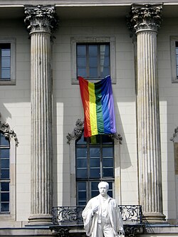 Regenbogenfahne vor dem Eingang der Humboldt-Universität zu Berlin, direkt neben einer Statue