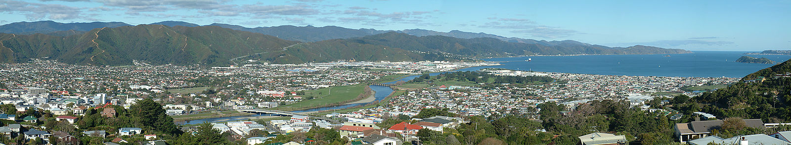 Lower Hutt from Normandale, in the western hills. On the right is the entrance to Wellington Harbour, with Matiu / Somes Island beneath. The Hutt River snakes from the right background to the left mid-ground, entering the harbour between the suburbs of Seaview and Petone. The Wainuiomata Hill Road climbs the hills in the centre background (the track in the middle of the left half of the background is a firebreak, not a road). At the foot of the Wainuiomata Hill Road is the Gracefield industrial area.