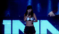 A photograph of Inna performing while wearing a black hat along with a black-white bra and shorts.