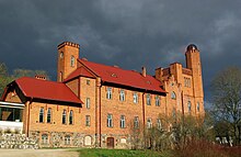 Photographie en couleurs d'une bâtisse illuminée de lumière chaude, se détachant sur fond de nuages gris